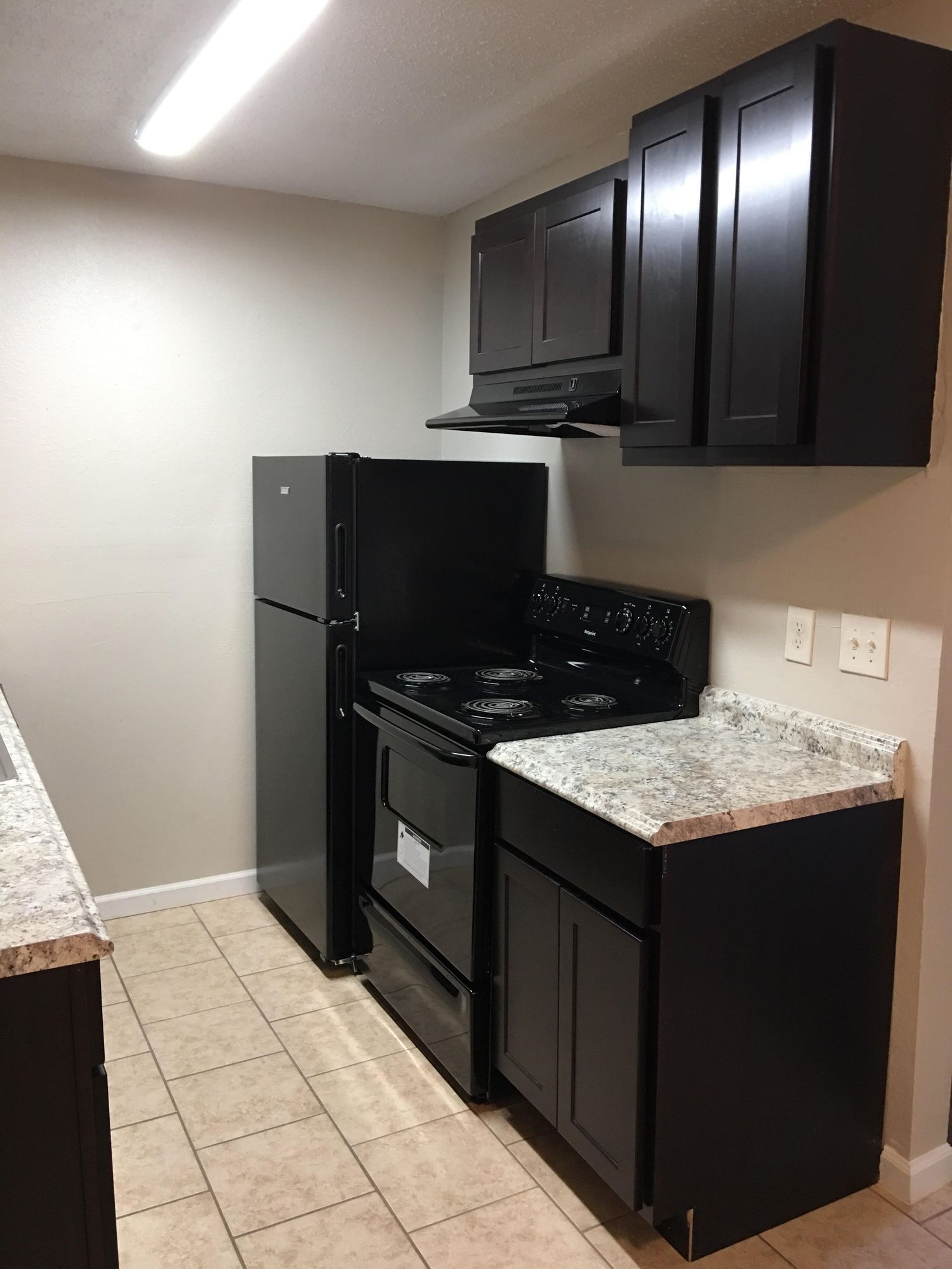 A small kitchen with black appliances and cabinets, beige tile, and a granite countertop.