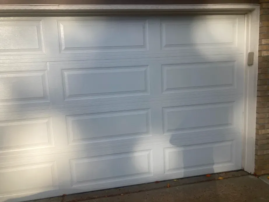 A white, multi-paneled residential garage door with a textured center strip, viewed from the exterior.