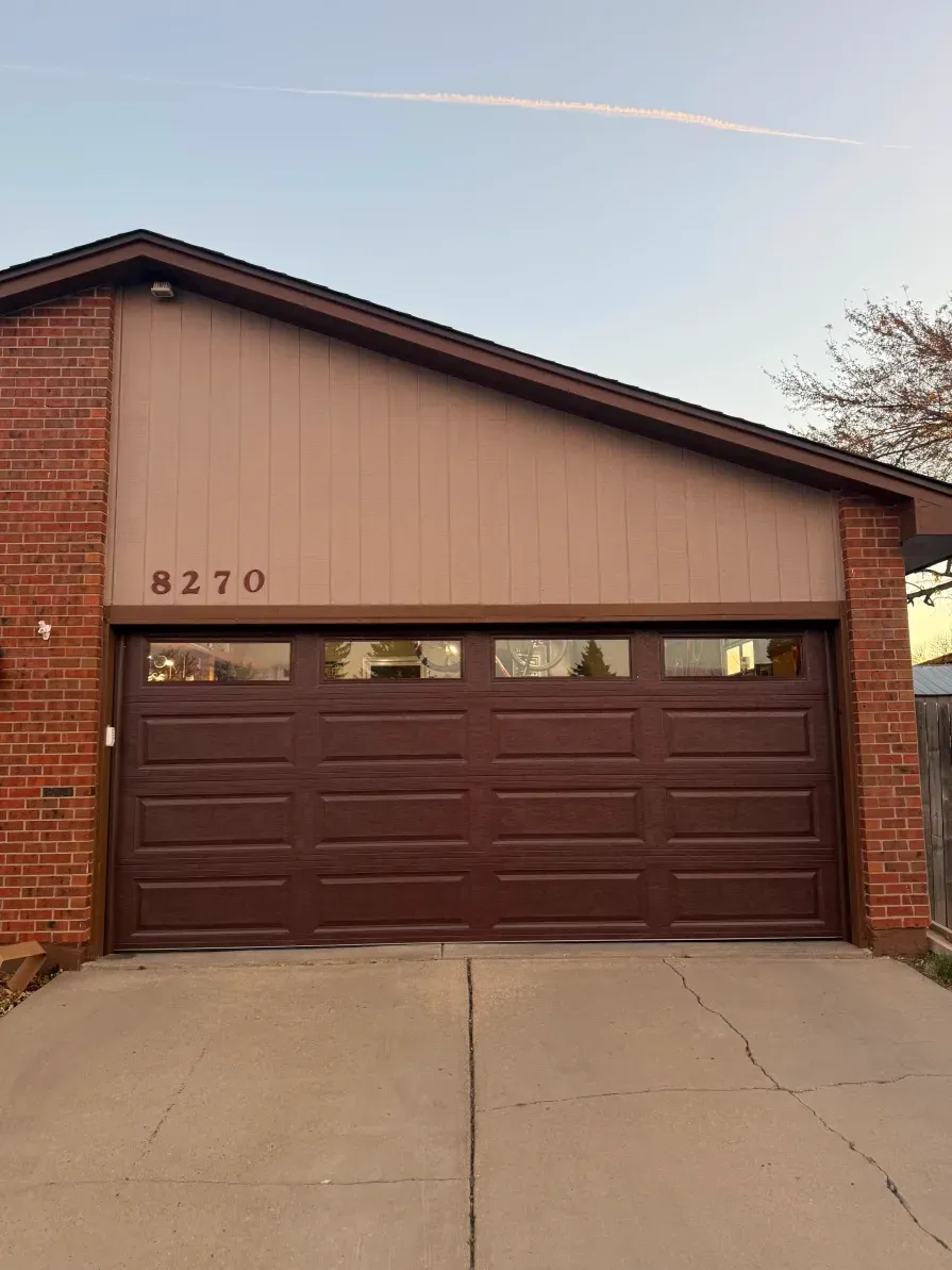 A single-story residential garage with brown paneled siding, a dark brown door with windows, and brick pillars.
