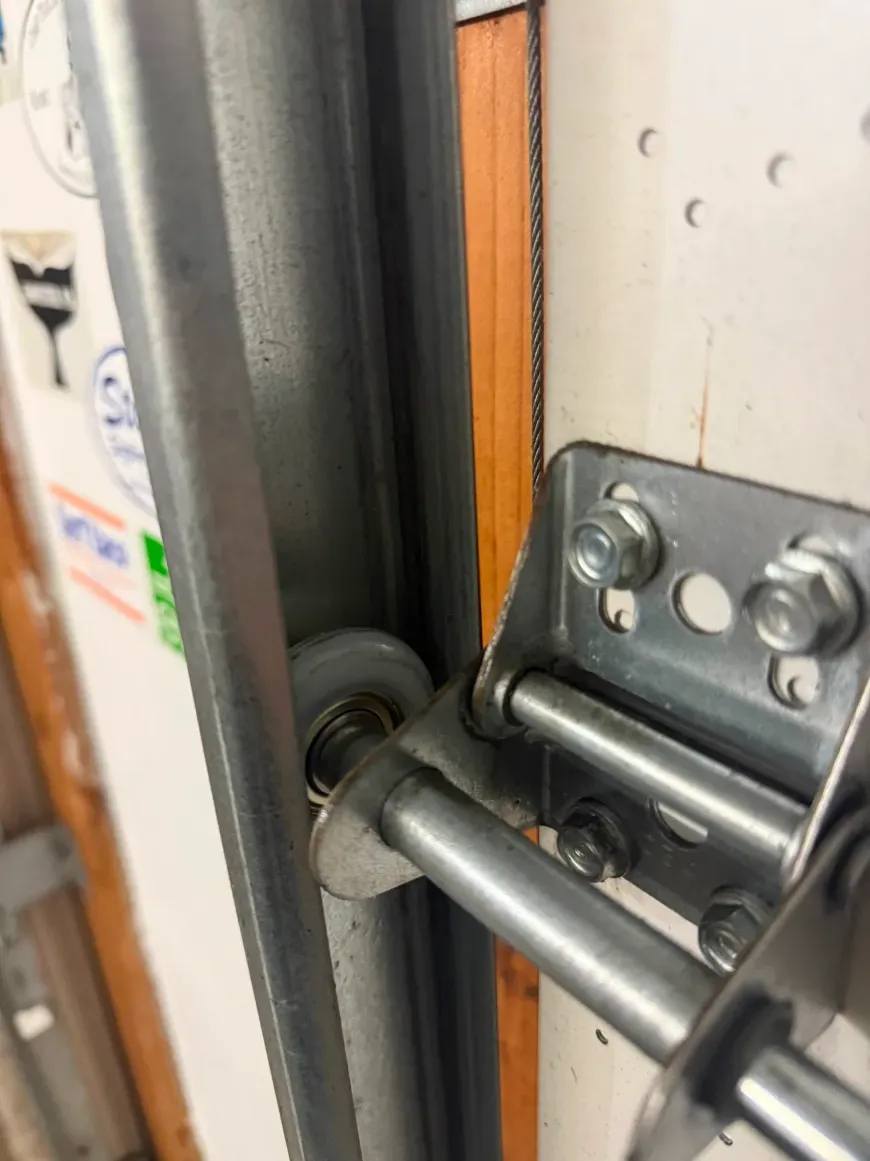 A close-up view of a metal garage door roller seated inside a vertical metal tracking rail.