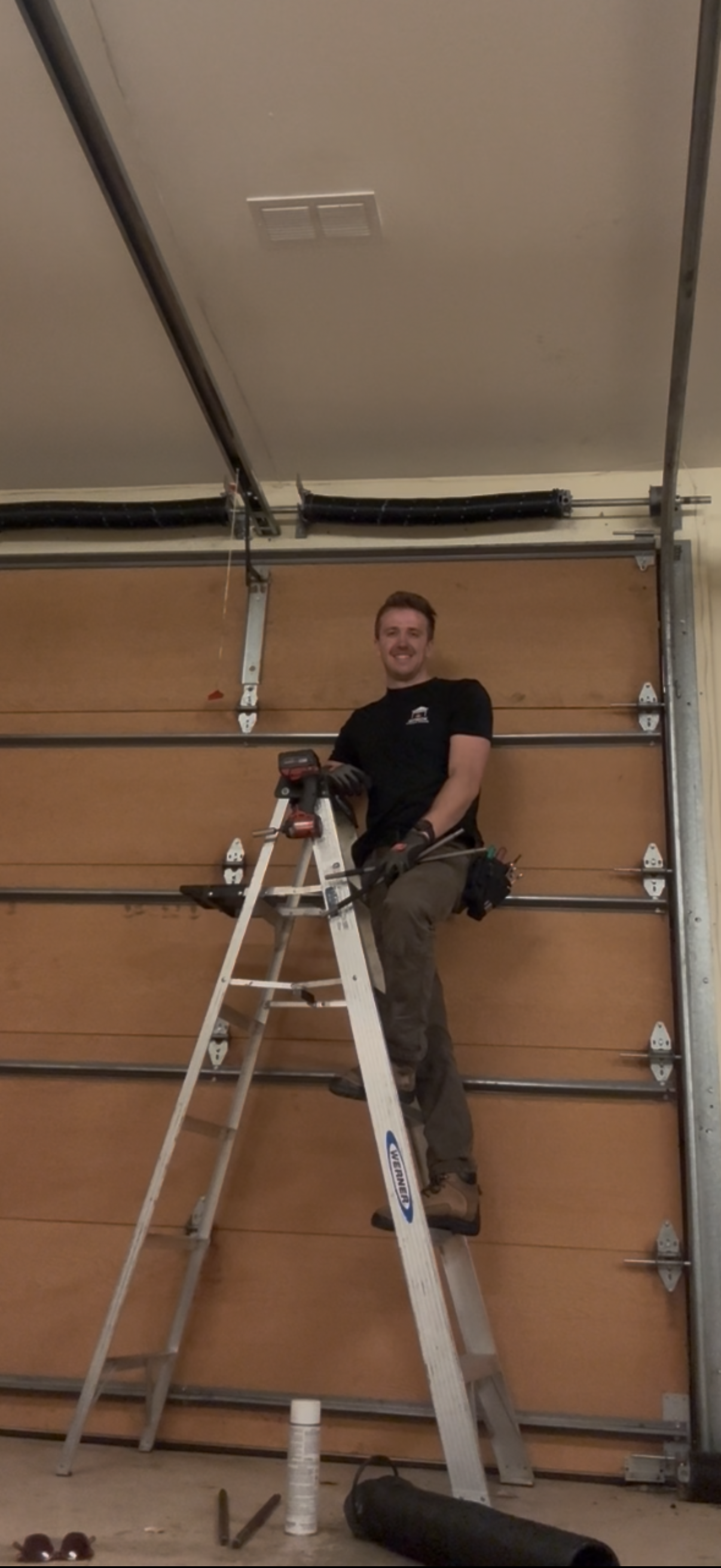 A detached garage with a white door, brown brick corners, and stucco gable, set on a concrete driveway under a blue sky.