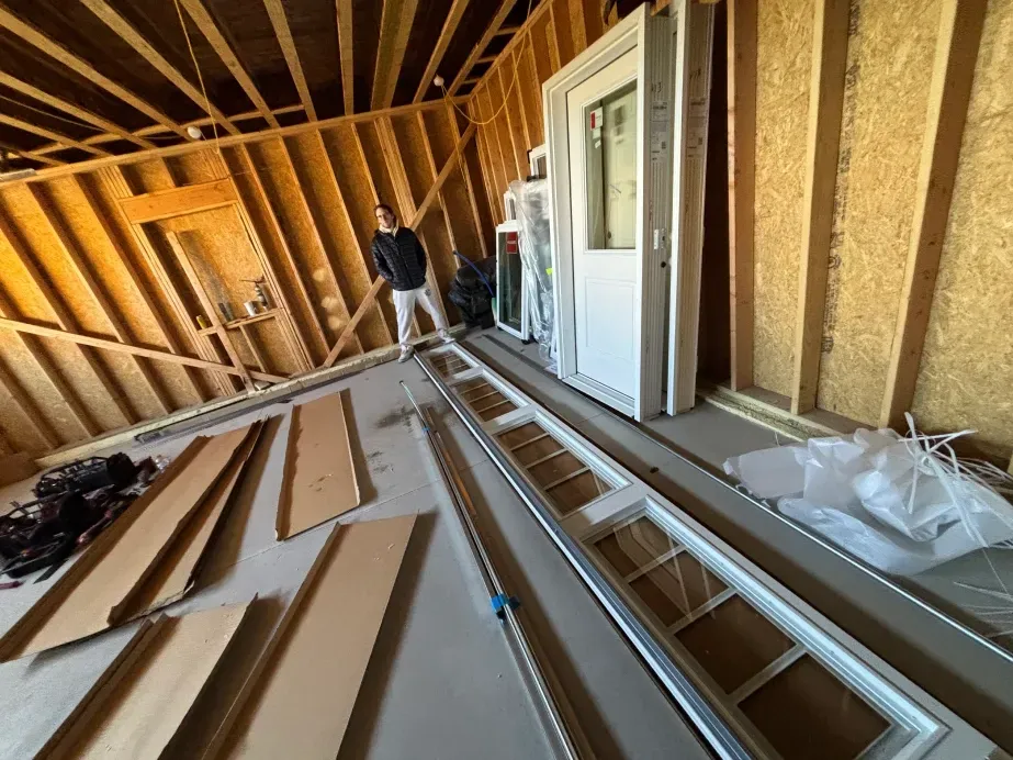A person stands in an unfinished, wood-framed building interior with doors and building materials laid on the floor.