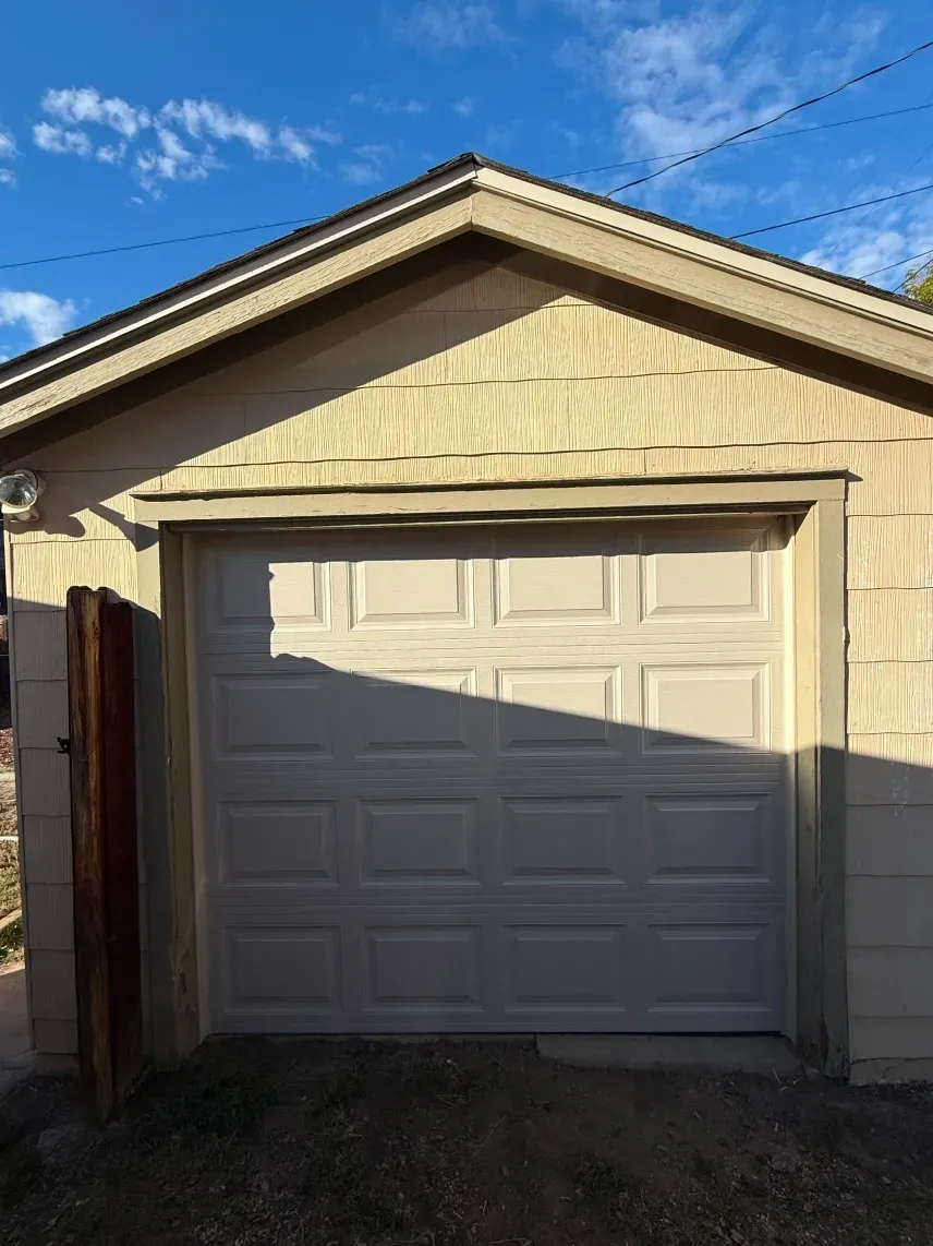 A white garage door with rectangular panels centered on a beige building under a blue sky.