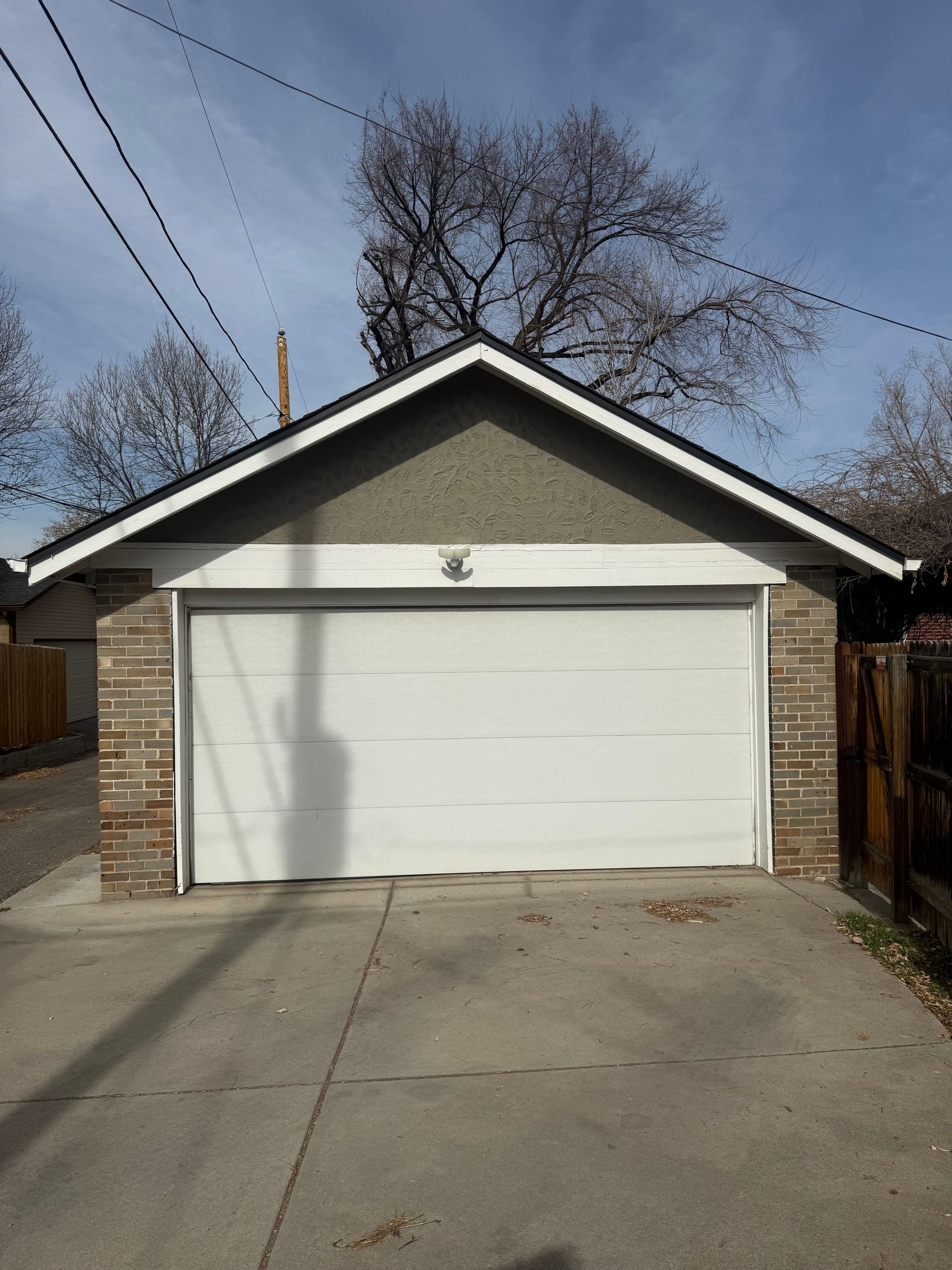 A detached garage with a white door, brown brick corners, and a grey stucco gable under a clear blue sky.