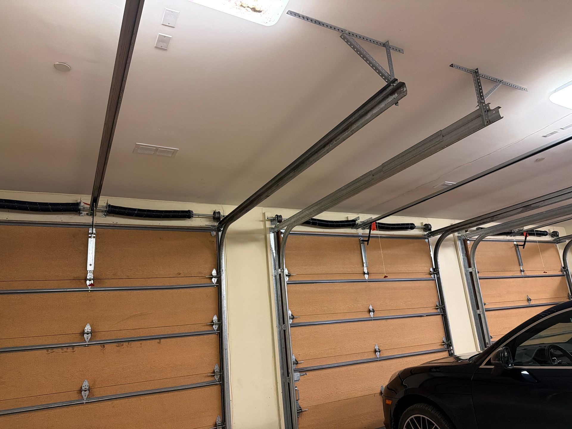 A view of the interior of a garage, showing ceiling-mounted garage door tracks, metal springs, and a parked car.