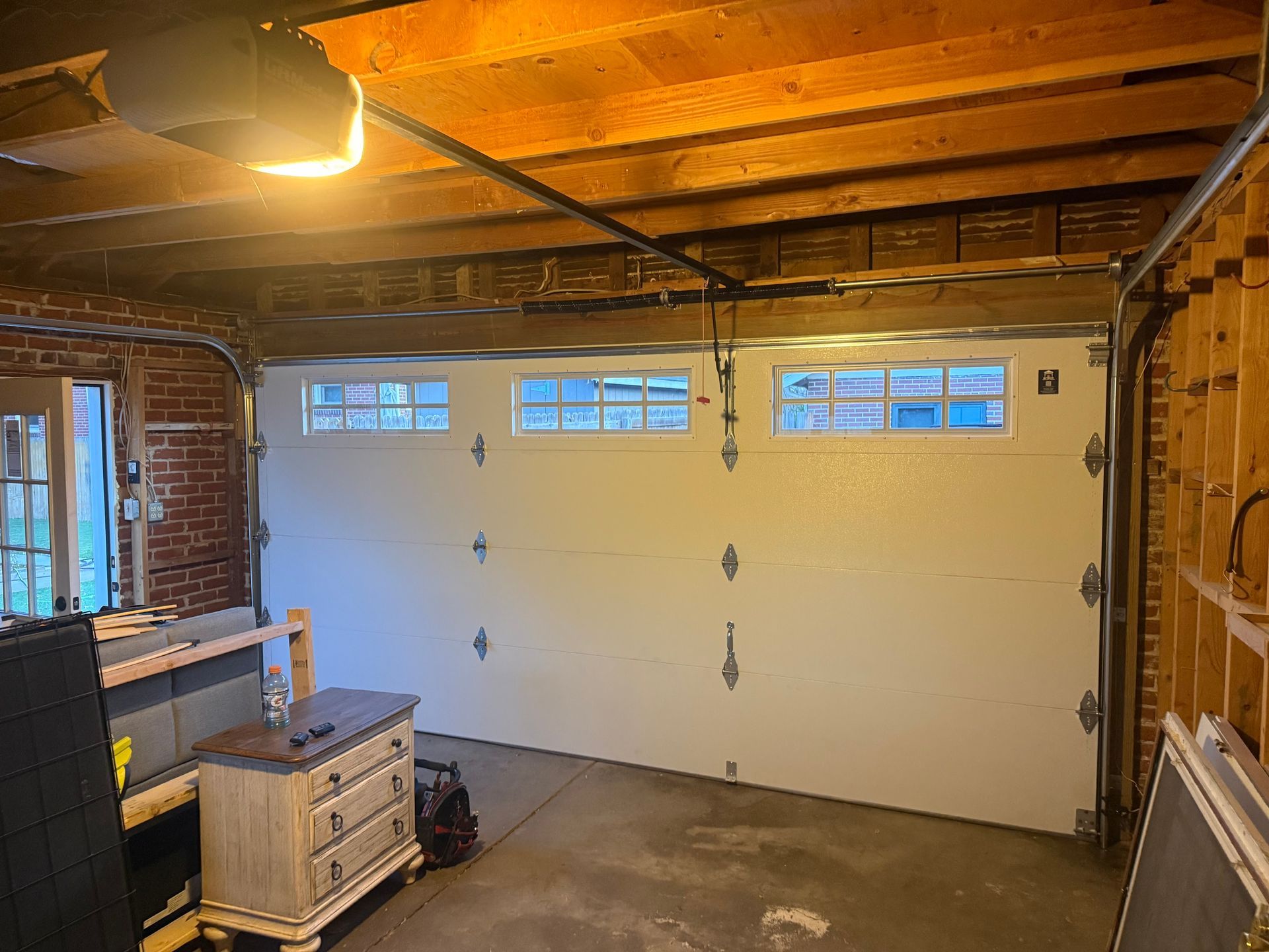 An interior view of a garage showing a closed white sectional garage door with three small, rectangular windows.