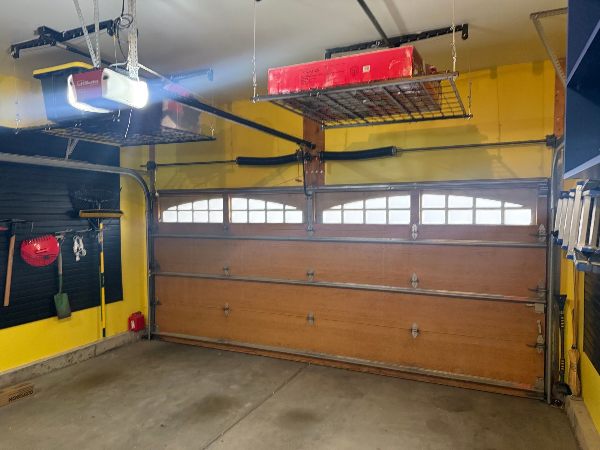 A garage interior featuring a wood-tone overhead door with windows, yellow walls, and a ceiling-mounted storage rack.