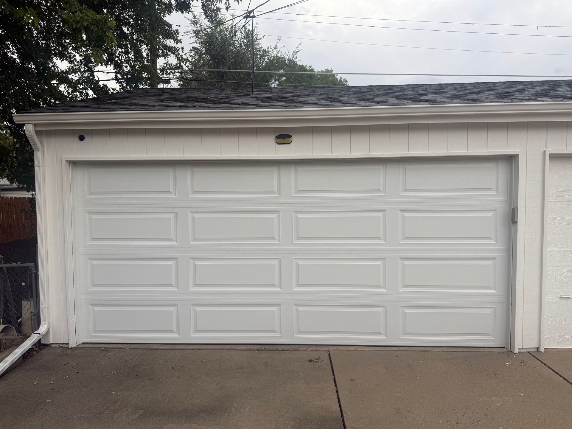 A white, four-panel residential garage door with rectangular recessed molding on an outdoor concrete driveway.