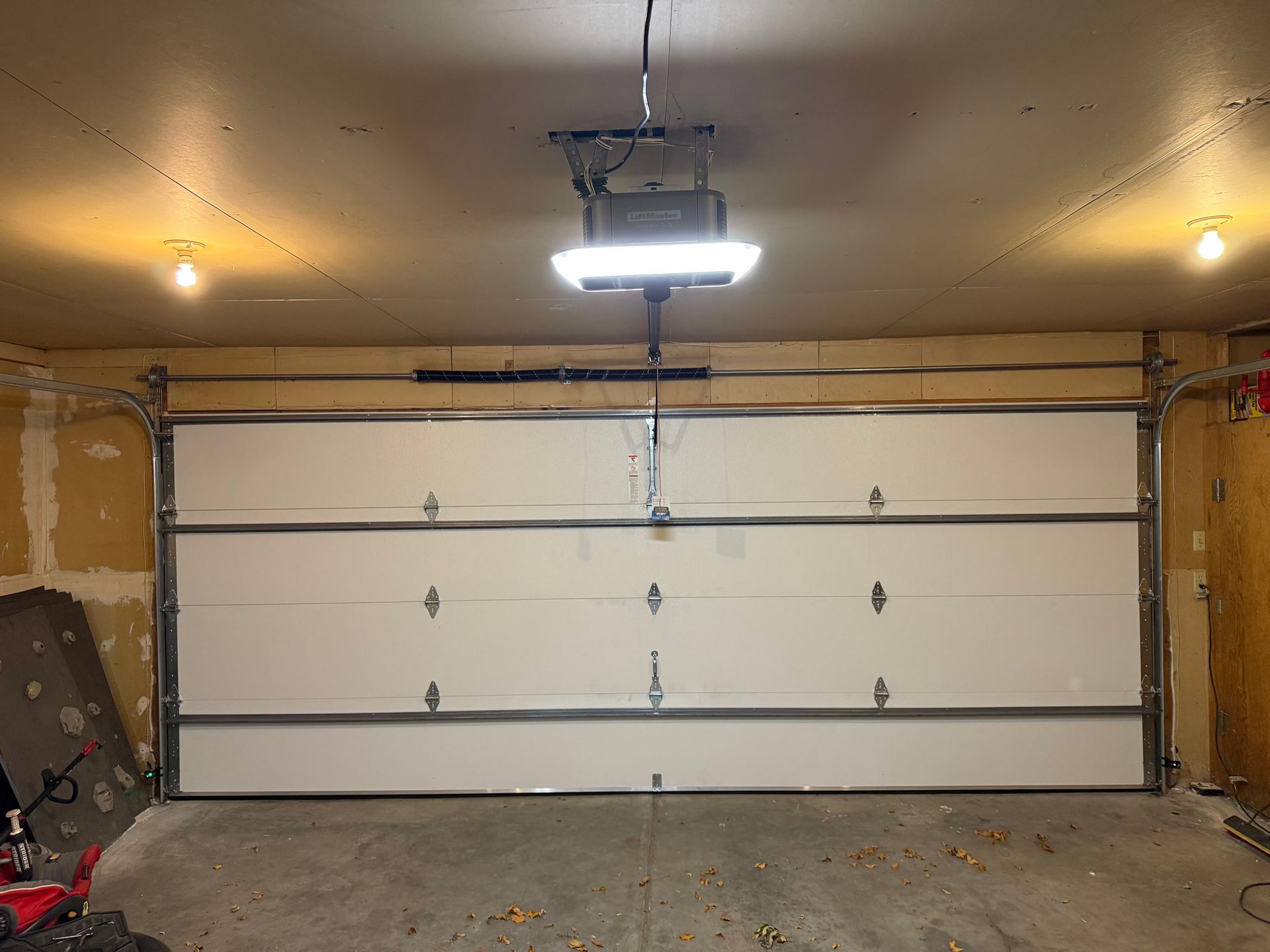 A closed white sectional garage door in a garage with a ceiling-mounted door opener and two overhead lights.