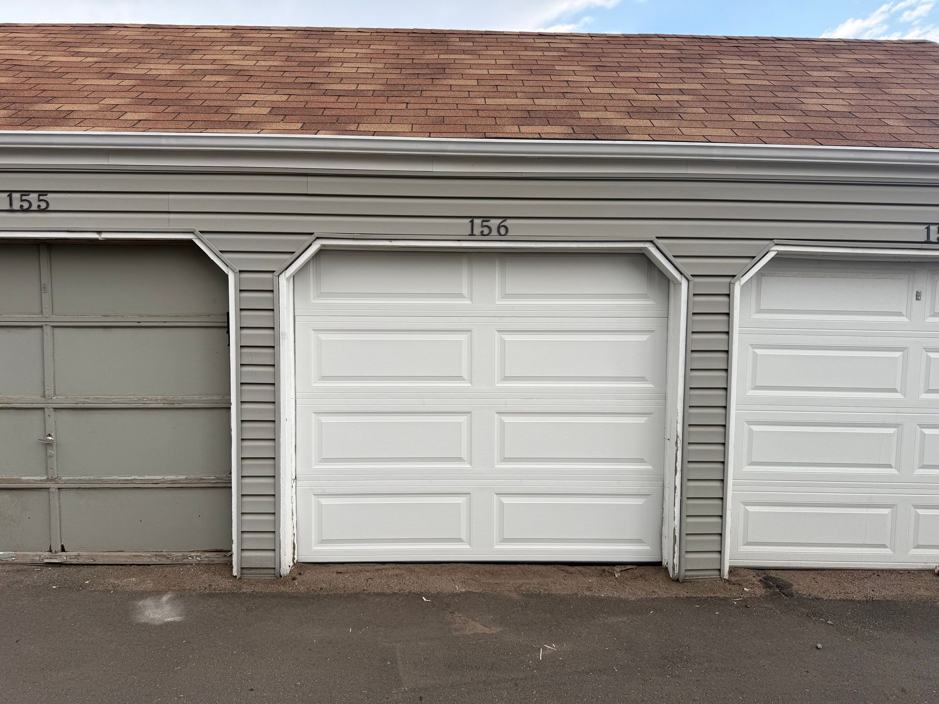 A row of garage doors labeled 155, 156, and 157 in a beige-sided building with a shingled roof.