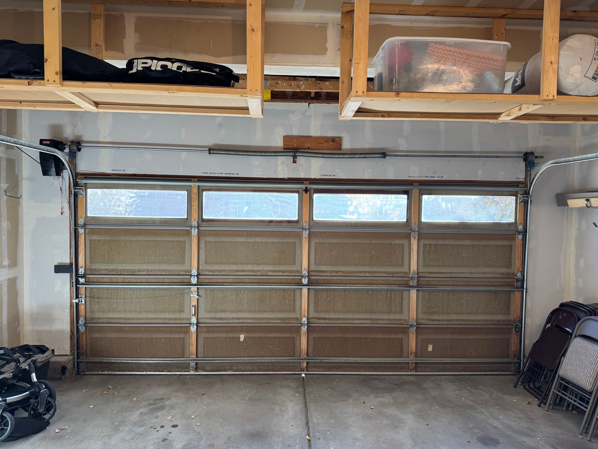 A closed garage door with windows, centered beneath wooden storage shelves holding various items.