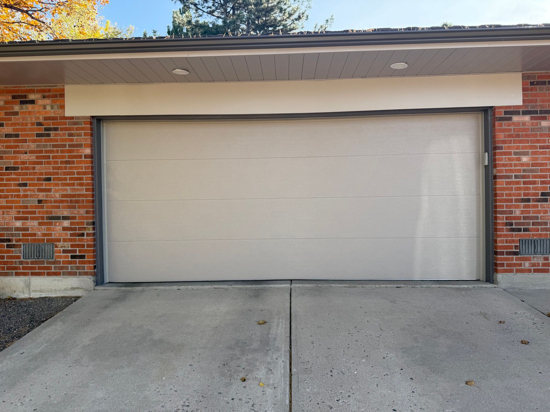 A beige, modern garage door on a brick home with a concrete driveway.