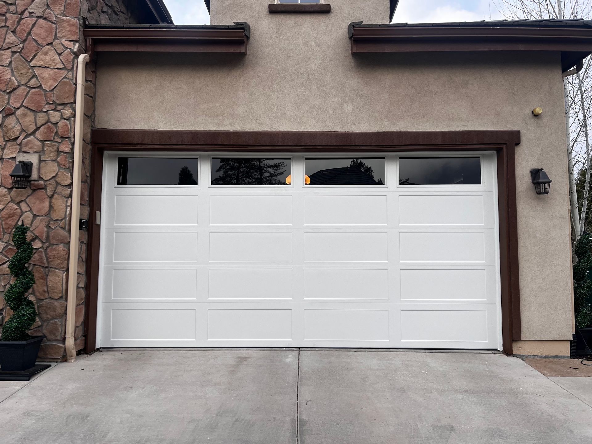 A white, four-panel garage door with top-row windows, set into a stucco building with stone siding.