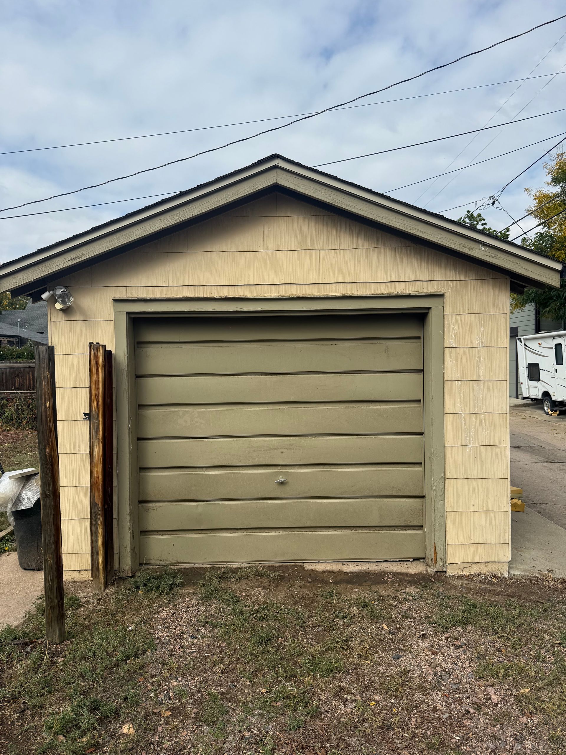 A detached, light tan garage with a weathered green roll-up door and a dark brown trim under an overcast sky.