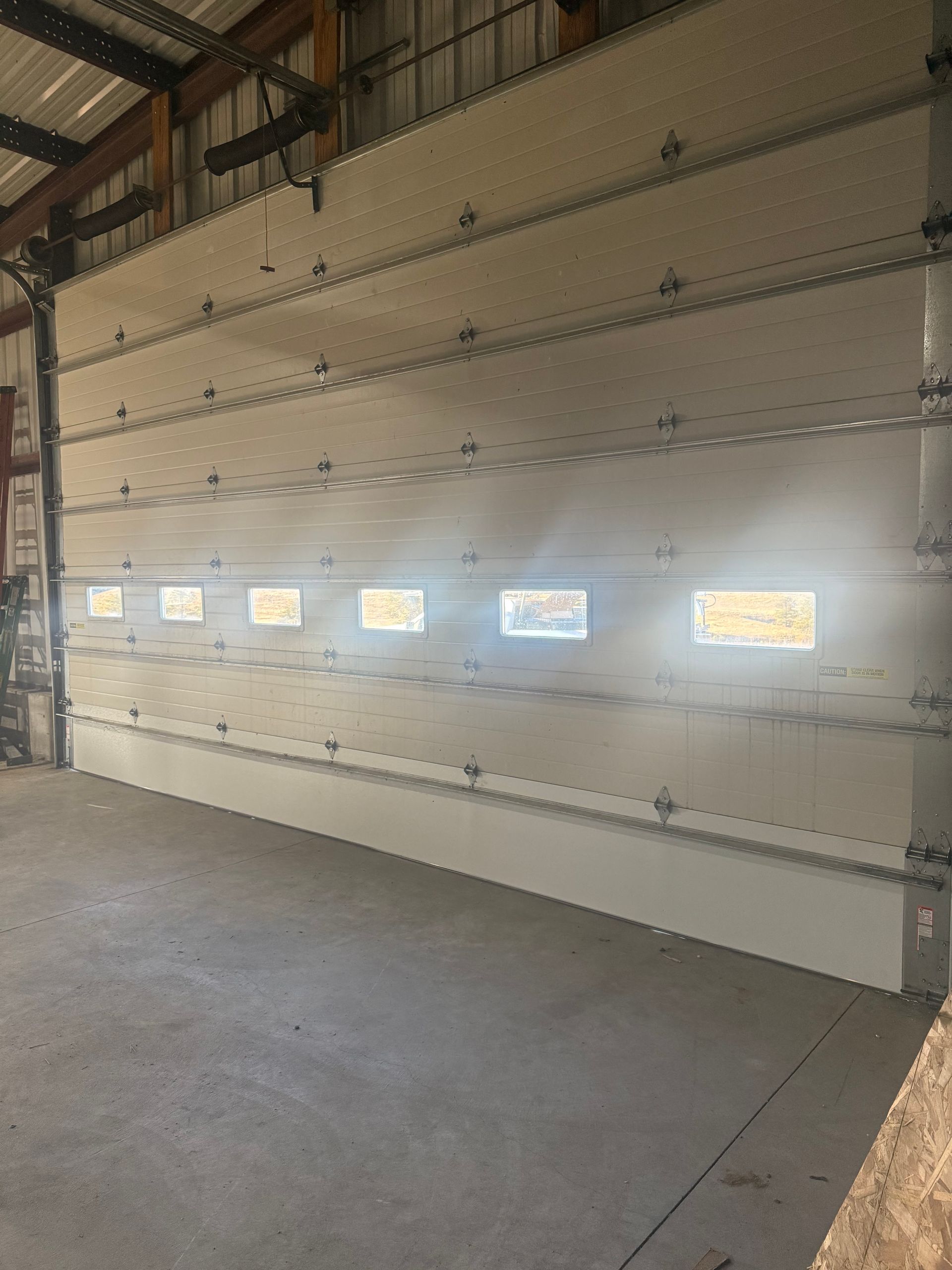 Interior view of a white, paneled garage door with a row of six rectangular windows and horizontal metal support bars.