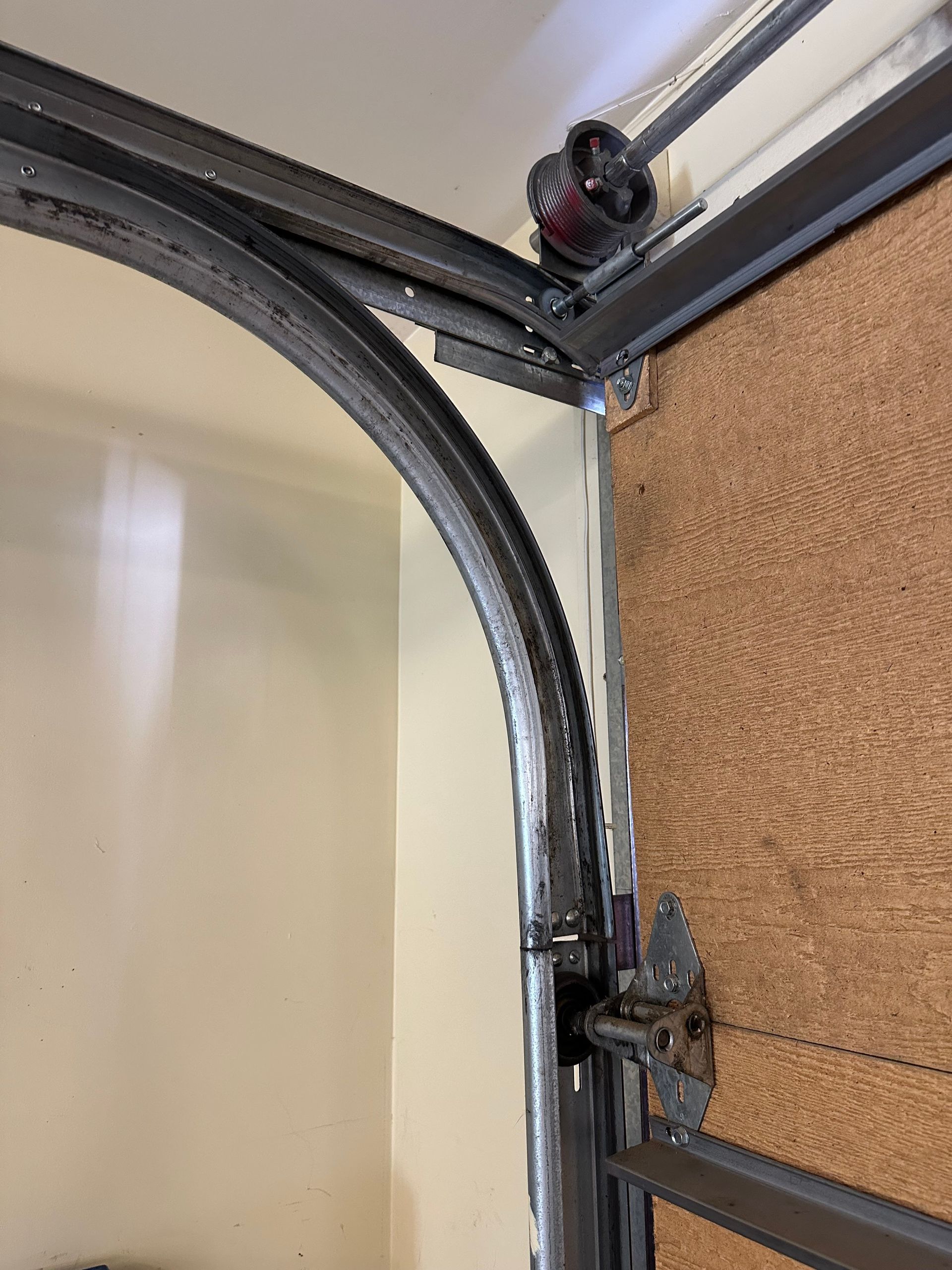 A view of a garage door track and roller mechanism where the metal roller has come off the track.