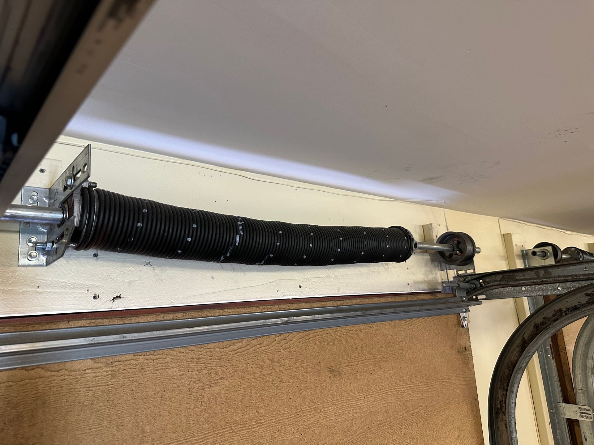 A black, coiled metal garage door torsion spring mounted horizontally on a wall above a door track.