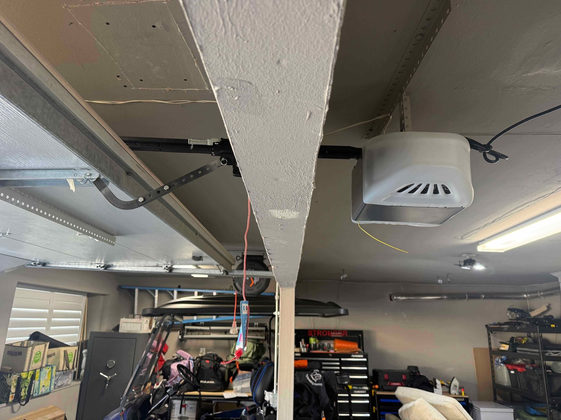 A garage ceiling view featuring a garage door opener motor, a support beam, and various storage items in the background.