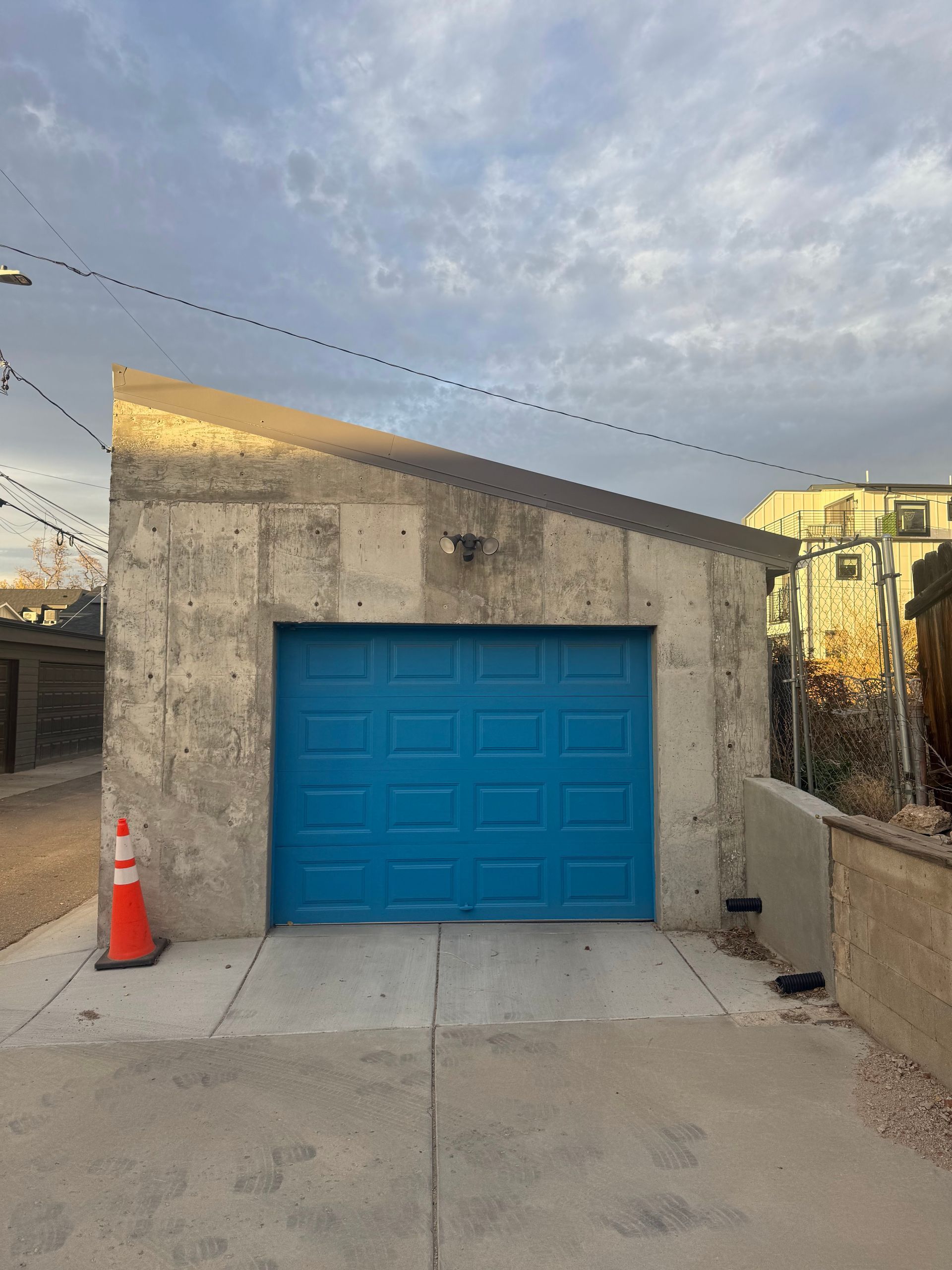 A single-car garage with a bright blue door and a slanted concrete roof, located in an outdoor alley setting.