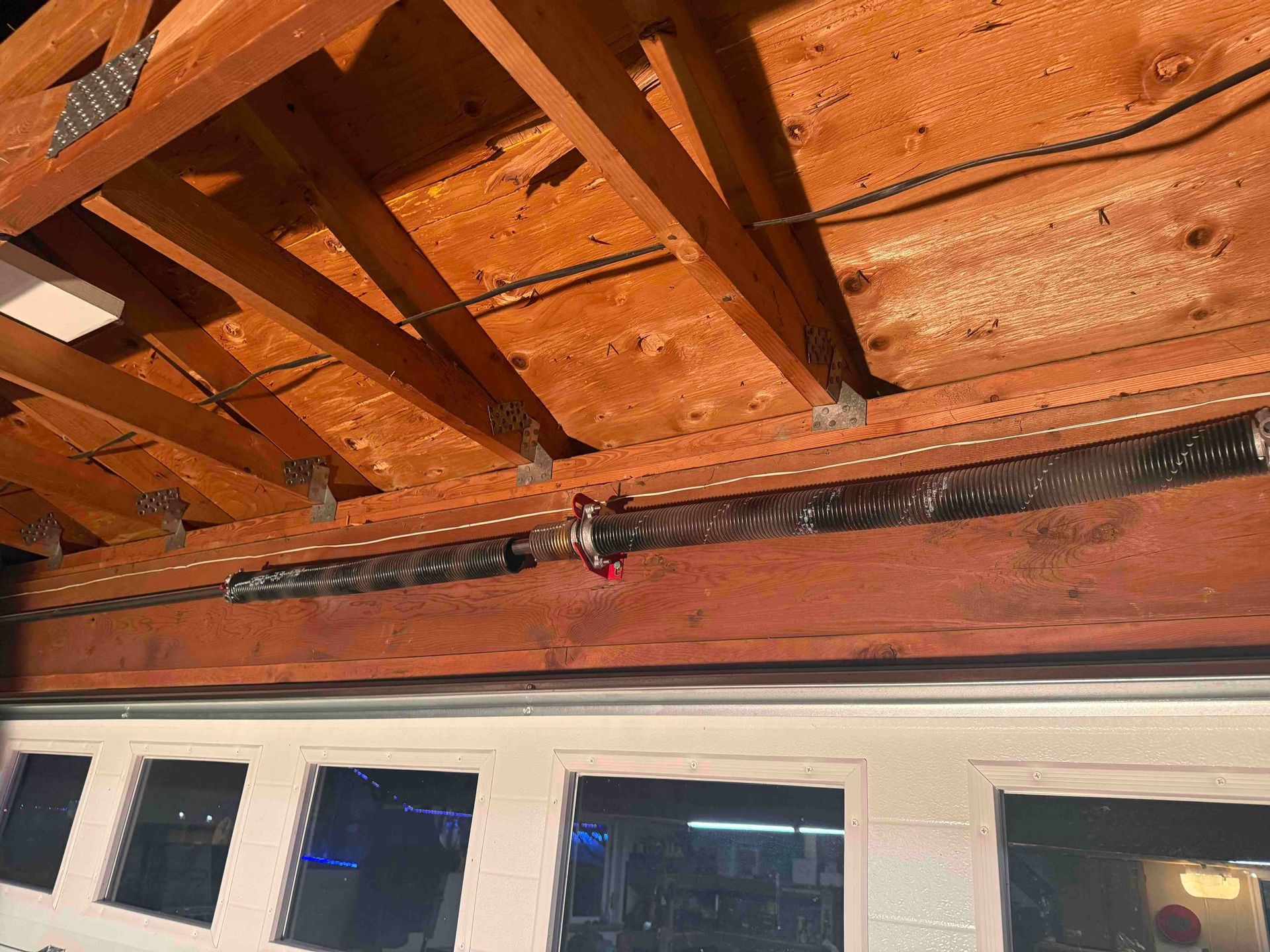 Torsion spring mechanism mounted on a wooden beam above a garage door.
