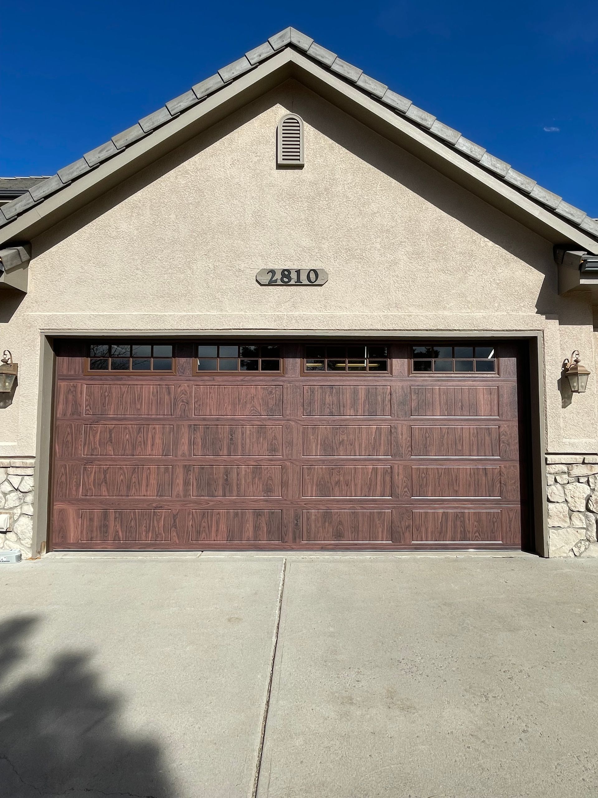 A tan home exterior featuring a dark wood-toned garage door with four windows and the number 7810 above it.