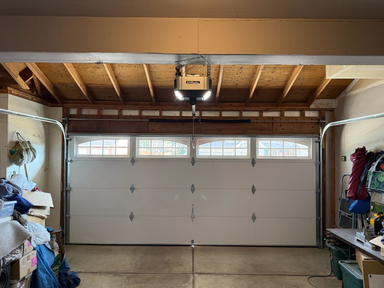 A white garage door with windows, featuring a central overhead door opener mounted to exposed wooden ceiling joists.