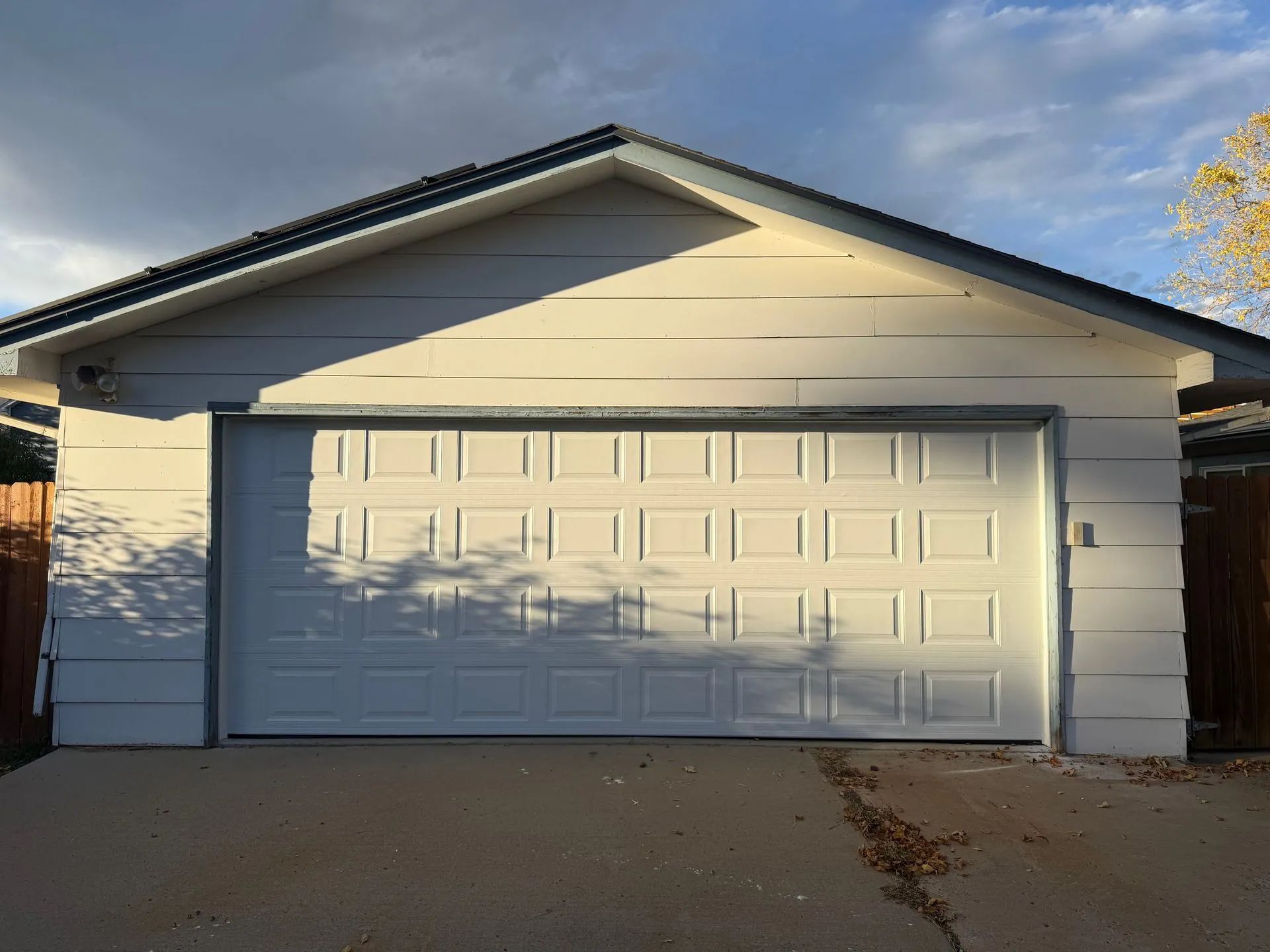 White detached garage with a white, rectangular-paneled roll-up door and a dark roof under a partially cloudy sky.