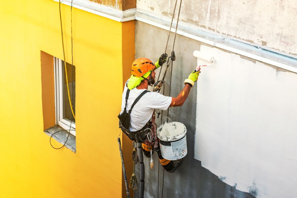 A Man is Painting the Side of a Building With a Roller — Axis Painting in Coffs Harbour, NSW