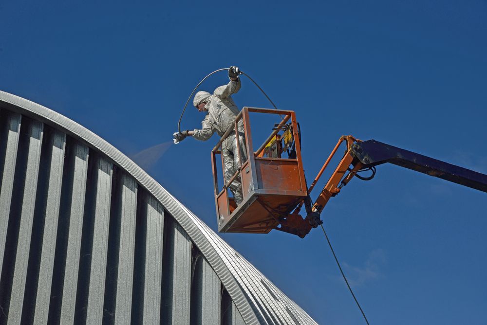 A Man is Spraying Paint From a Crane on Top of a Building — Axis Painting in Coffs Harbour, NSW