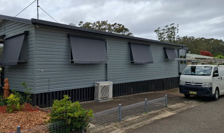 A white van is parked in front of a house with awnings on the windows — Axis Painting in Coffs Harbour, NSW