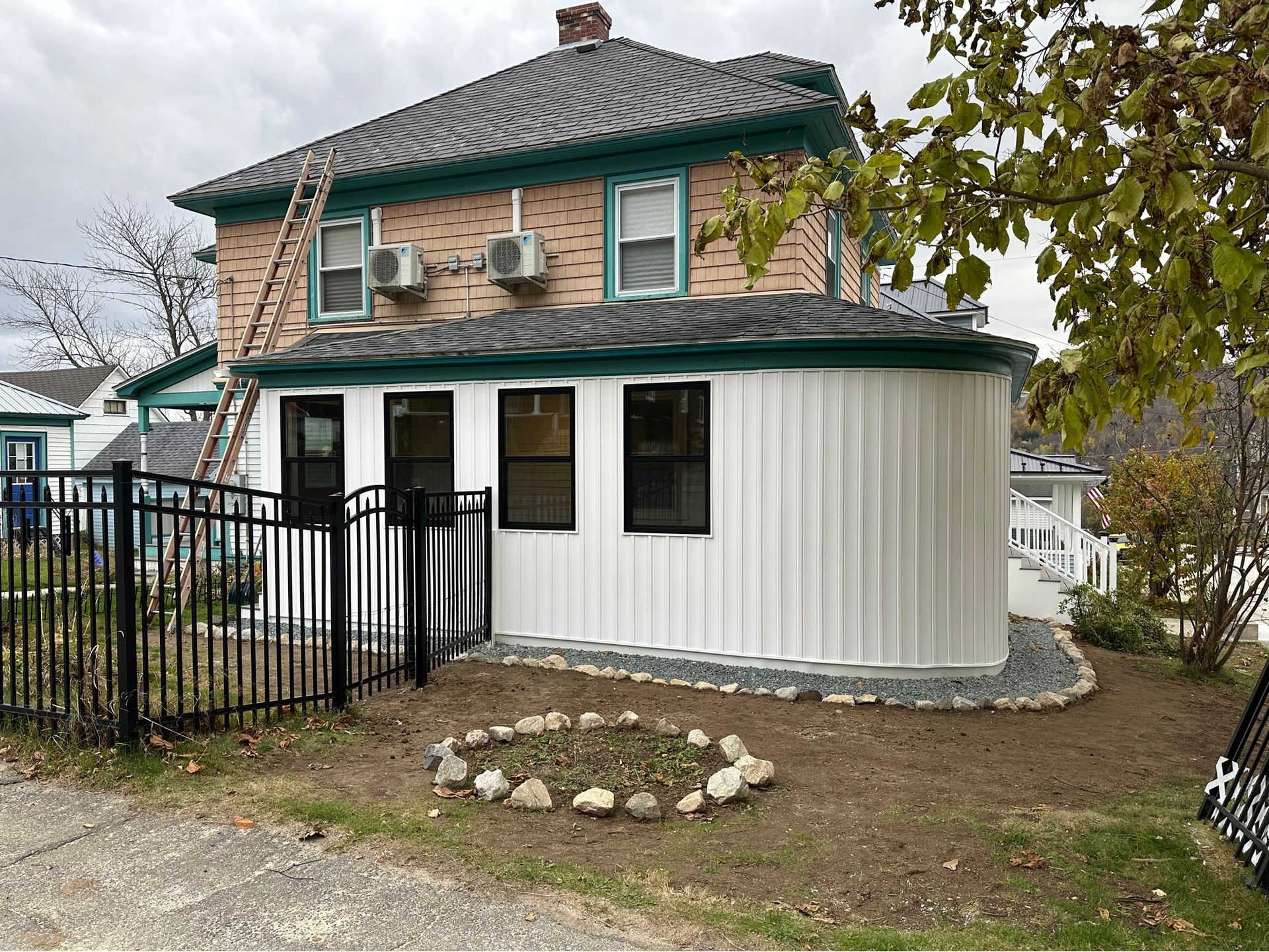 Two-story brick house with white siding, green roof, and black fenced yard in a suburban neighborhood