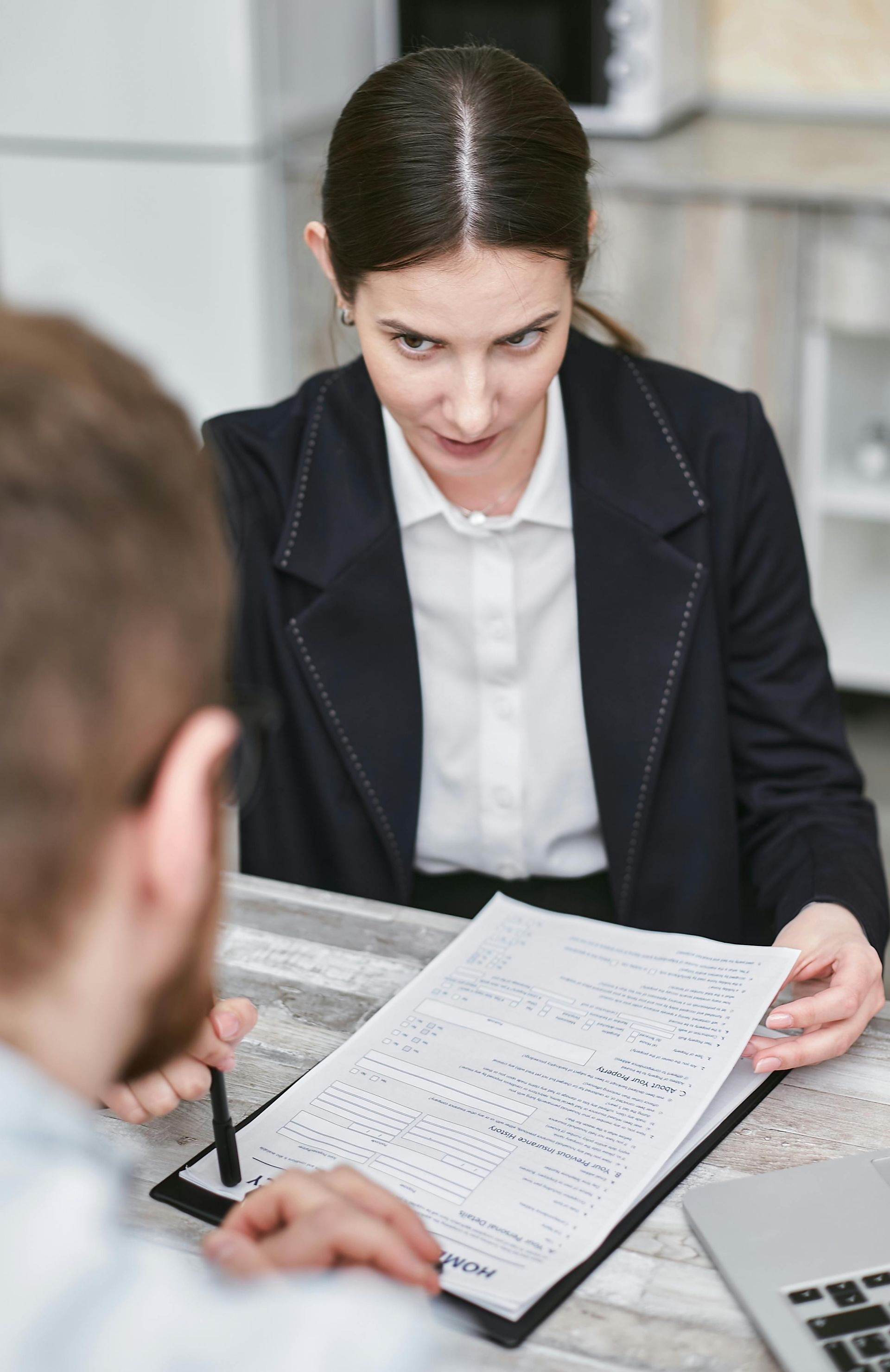 Woman in blazer reviews document with man across a table; indoor setting.