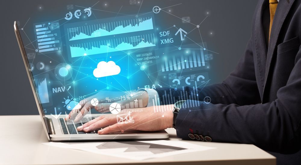 A person in a suit working on a laptop displaying data visualizations and a cloud icon.