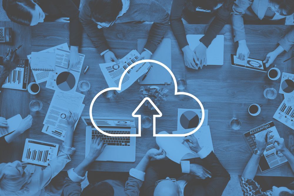 Business team around a table, with a cloud upload icon overlayed.
