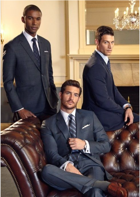 Three men in suits pose, one seated on a leather sofa. They wear ties, in an elegant interior setting. Three men in suits pose, one seated on a leather sofa. They wear ties, in an elegant interior setting.