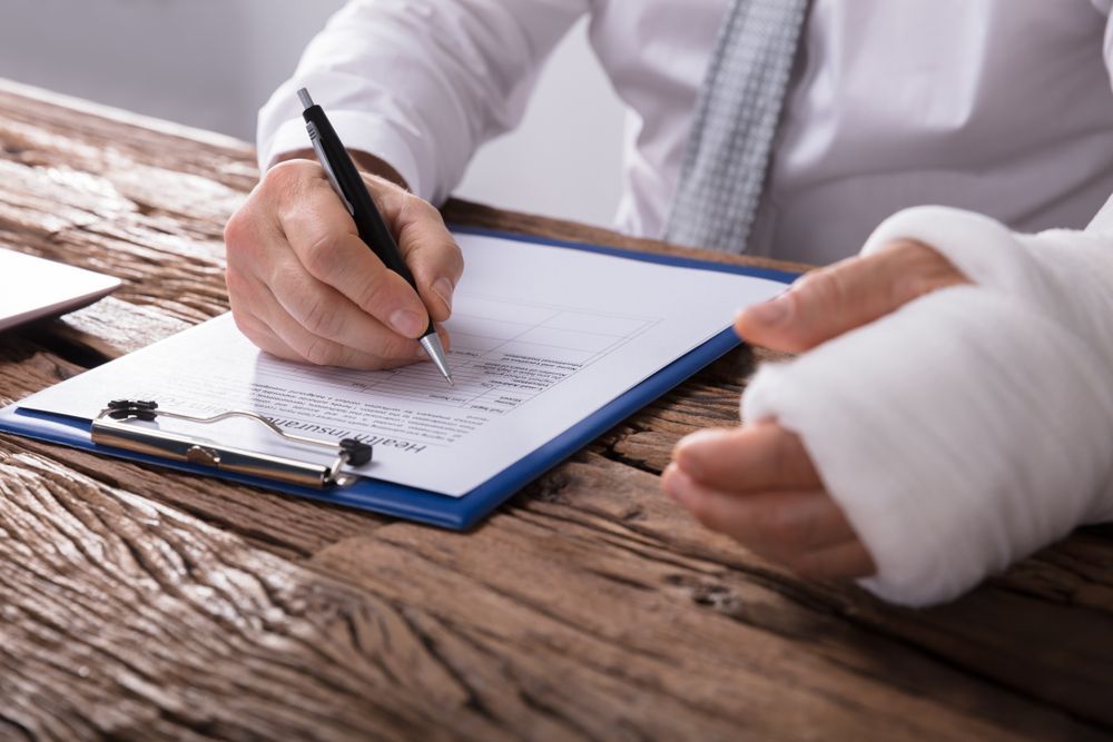 Person With Bandaged Wrist Writing on a Clipboard at a Wooden Desk — Umbrella Legal in Cardiff, NSW
