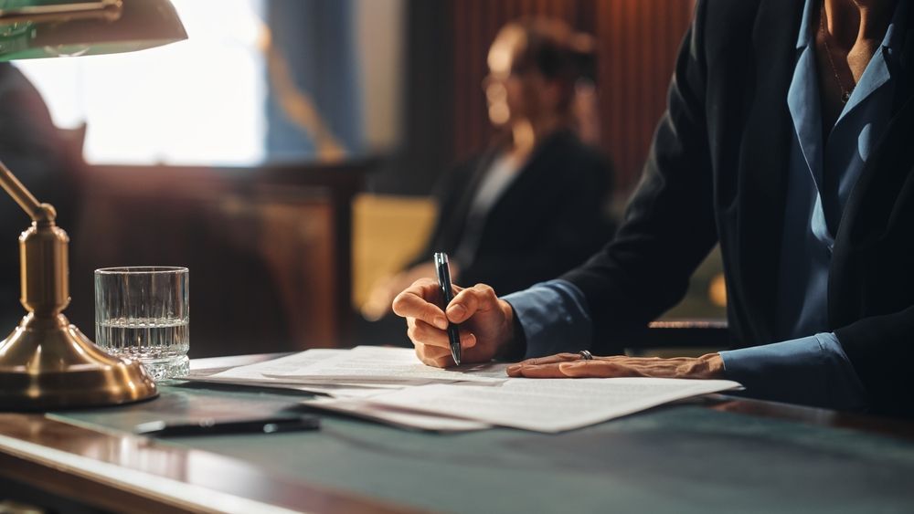 Person Writing at Desk With Papers, Glass of Water — Umbrella Legal in Cardiff, NSW