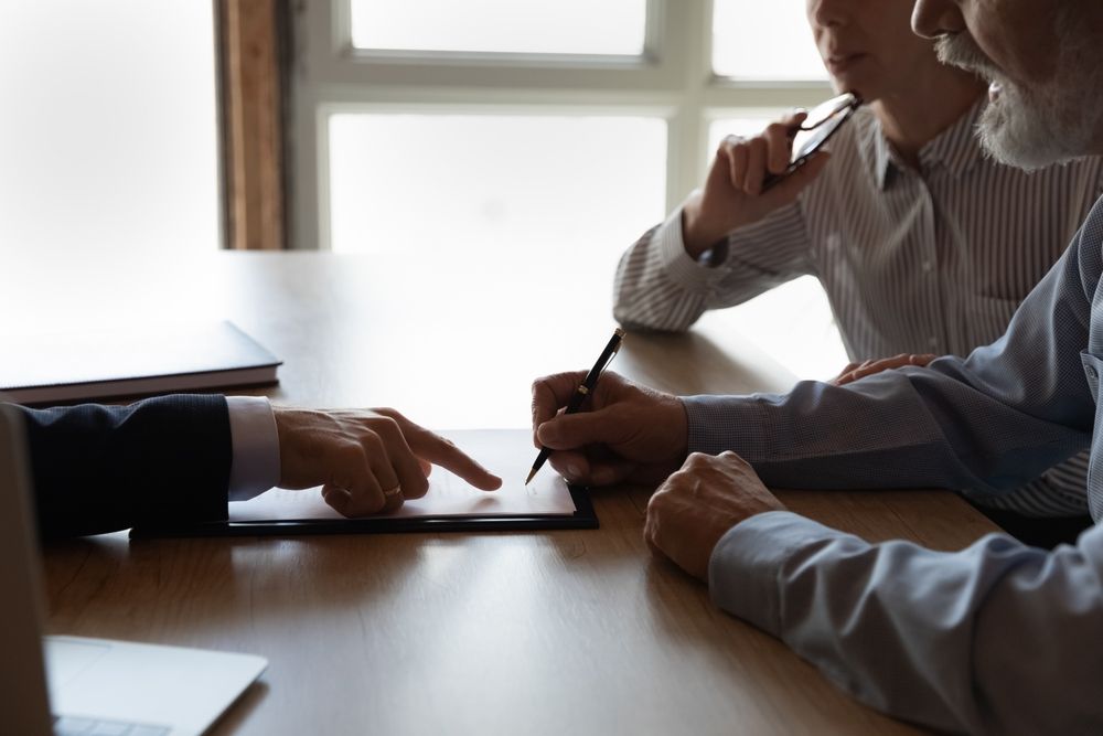 People in a meeting pointing at papers on a wooden table by a window