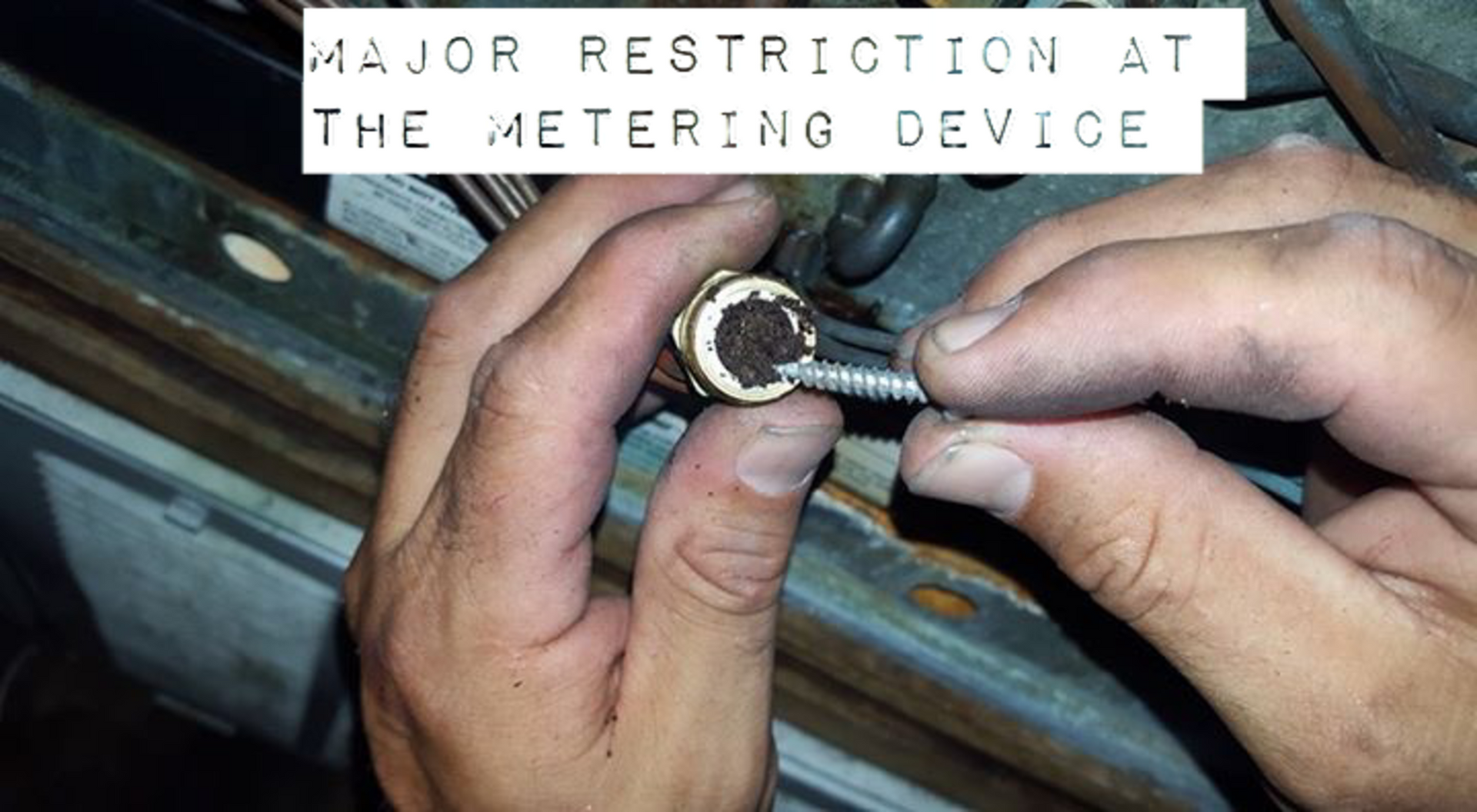 A person is holding a screw in their hand with a sign that says major restriction at the metering device