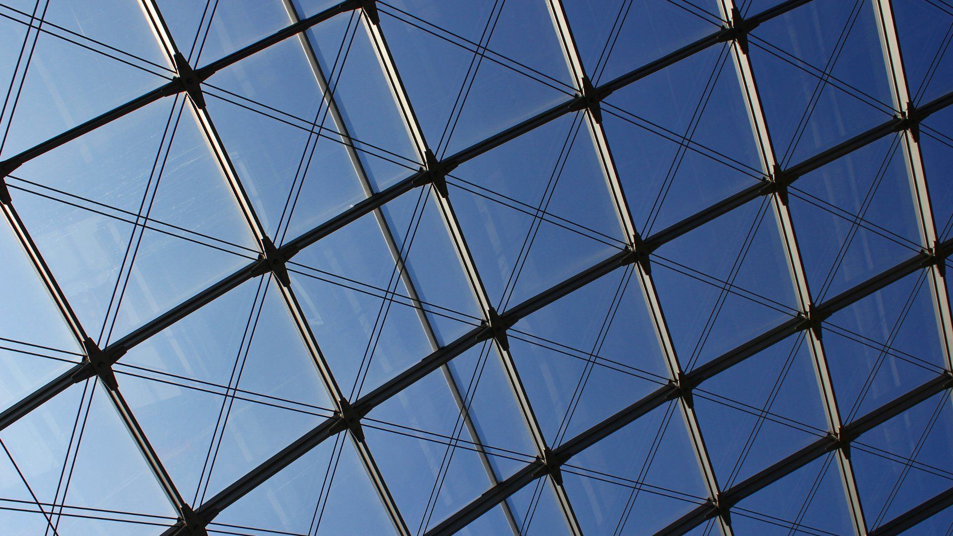 Geometric glass and metal ceiling with blue sky visible through triangular panes