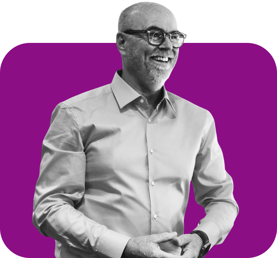 A smiling person in a light-colored button-down shirt and glasses, set against a solid purple background.