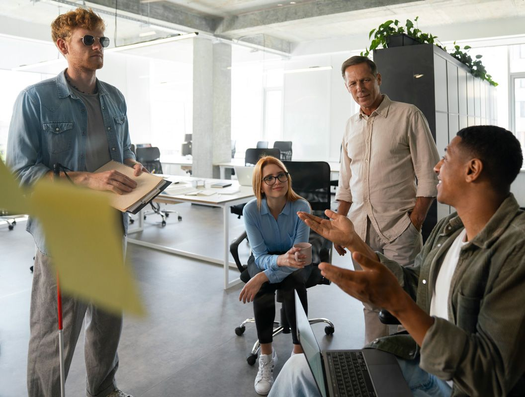 Coworkers discussing ideas in a bright modern office, with one person presenting and others seated and standing nearby