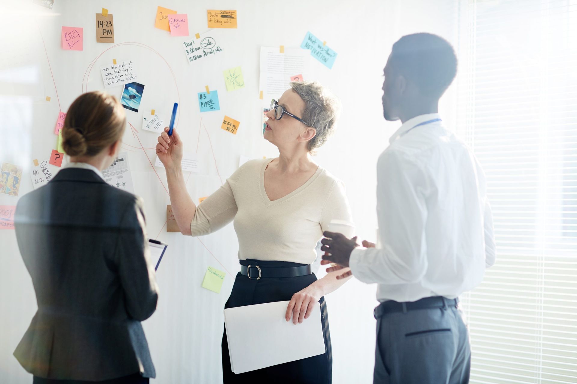 Three coworkers discuss notes on a whiteboard in a bright office.