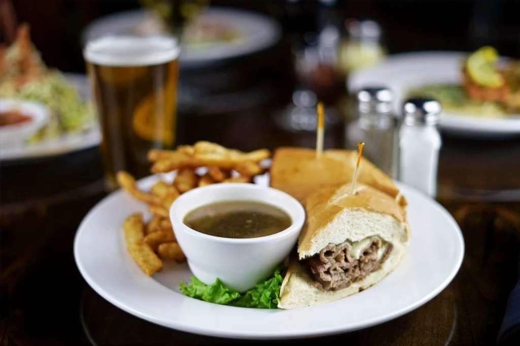 French dip sandwich with au jus and french fries on a table.