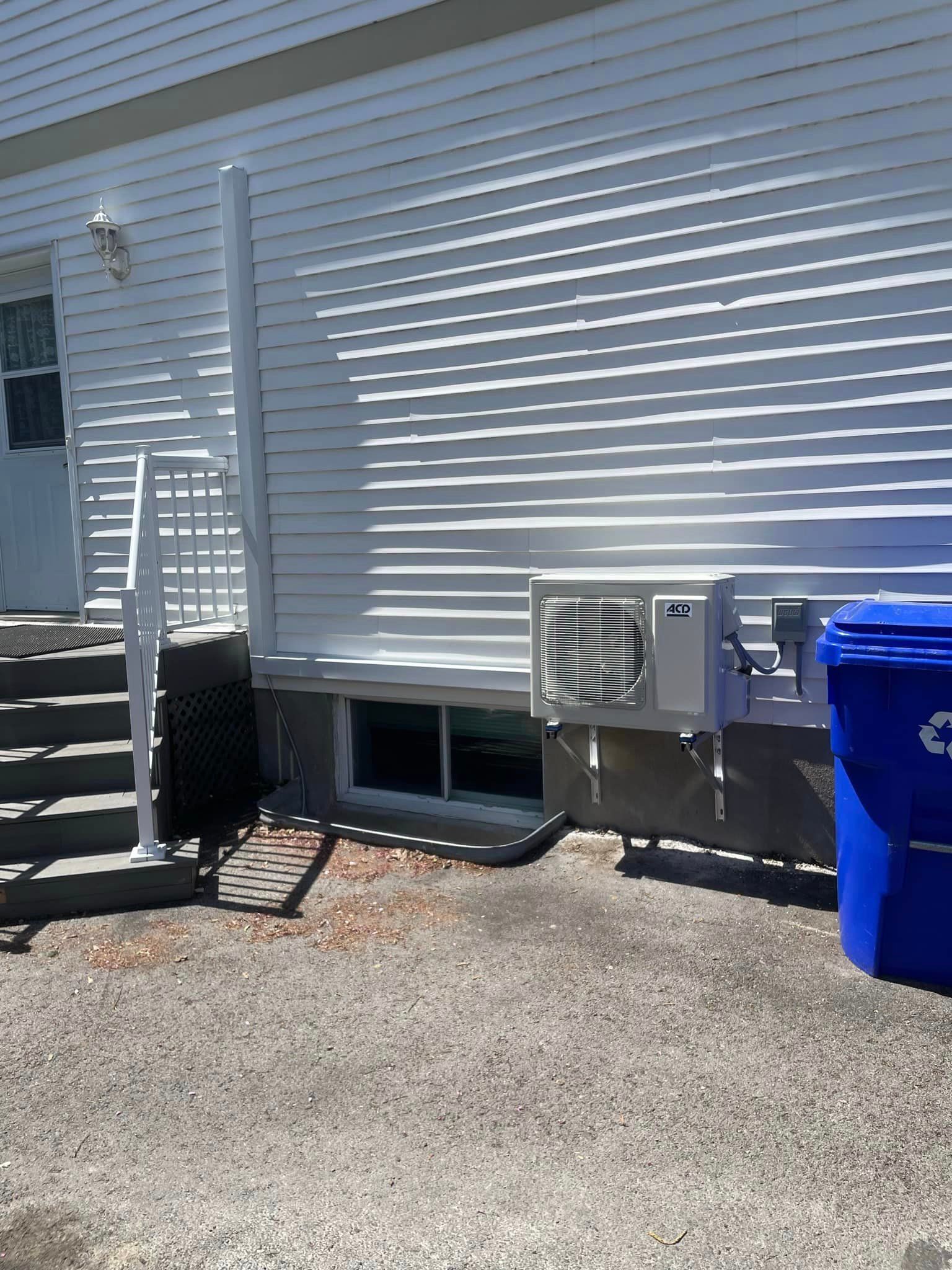 Une maison blanche avec une poubelle bleue devant.