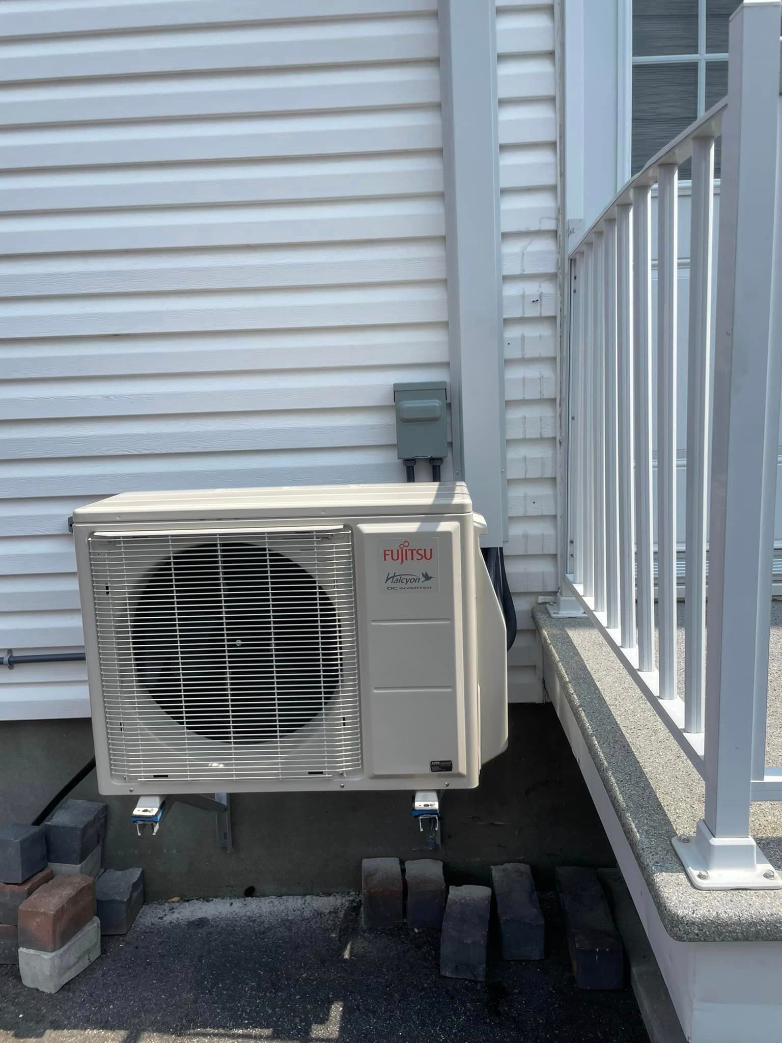 Un climatiseur blanc est posé sur le côté d'une maison à côté d'une balustrade.