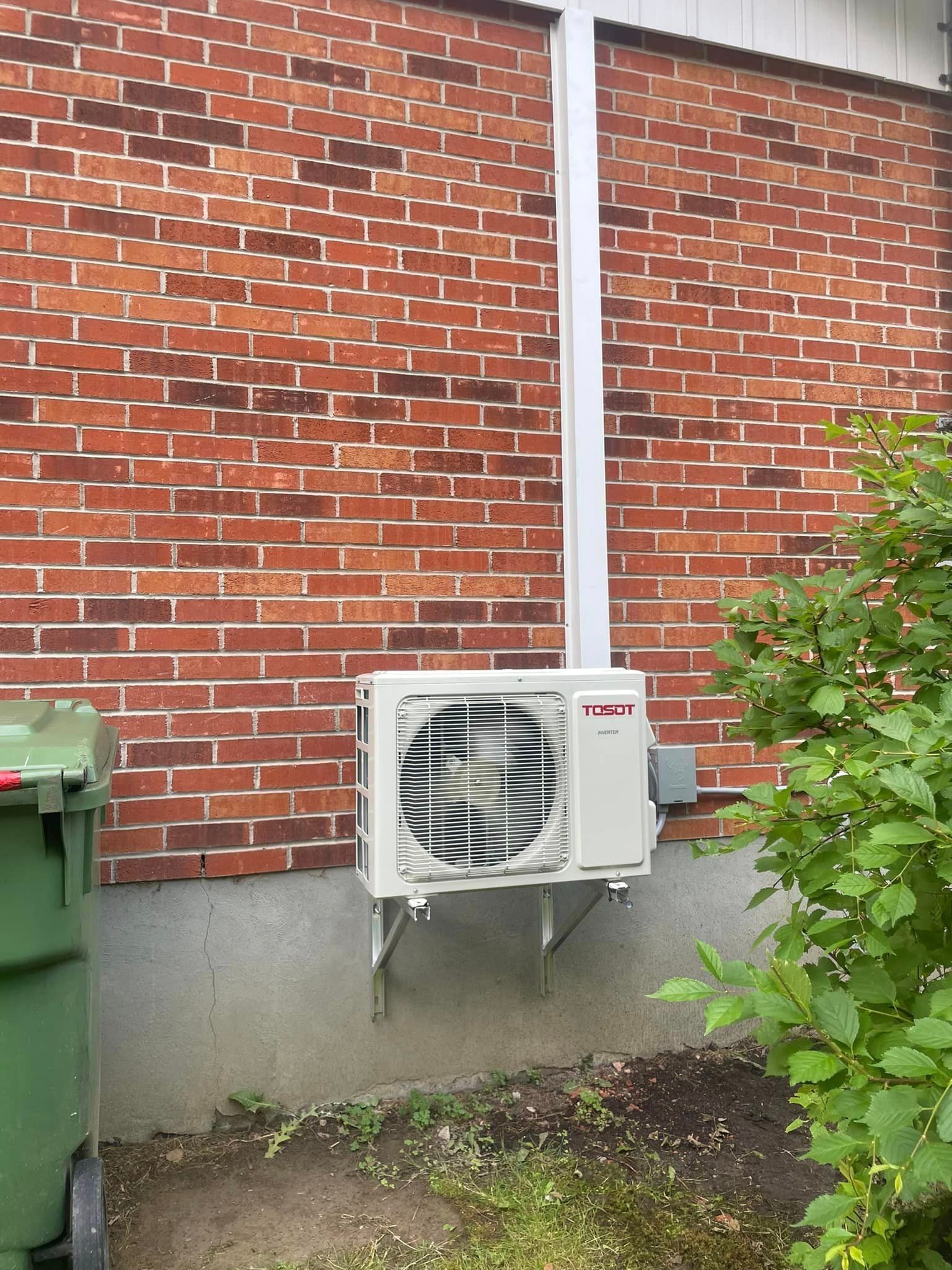 Un climatiseur blanc est monté sur le côté d'un bâtiment en briques.