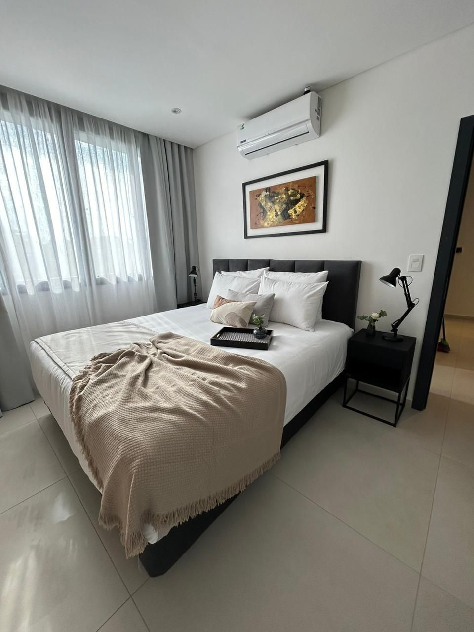 Dormitorio moderno con cama, manta, obra de arte y mesita de noche negra.