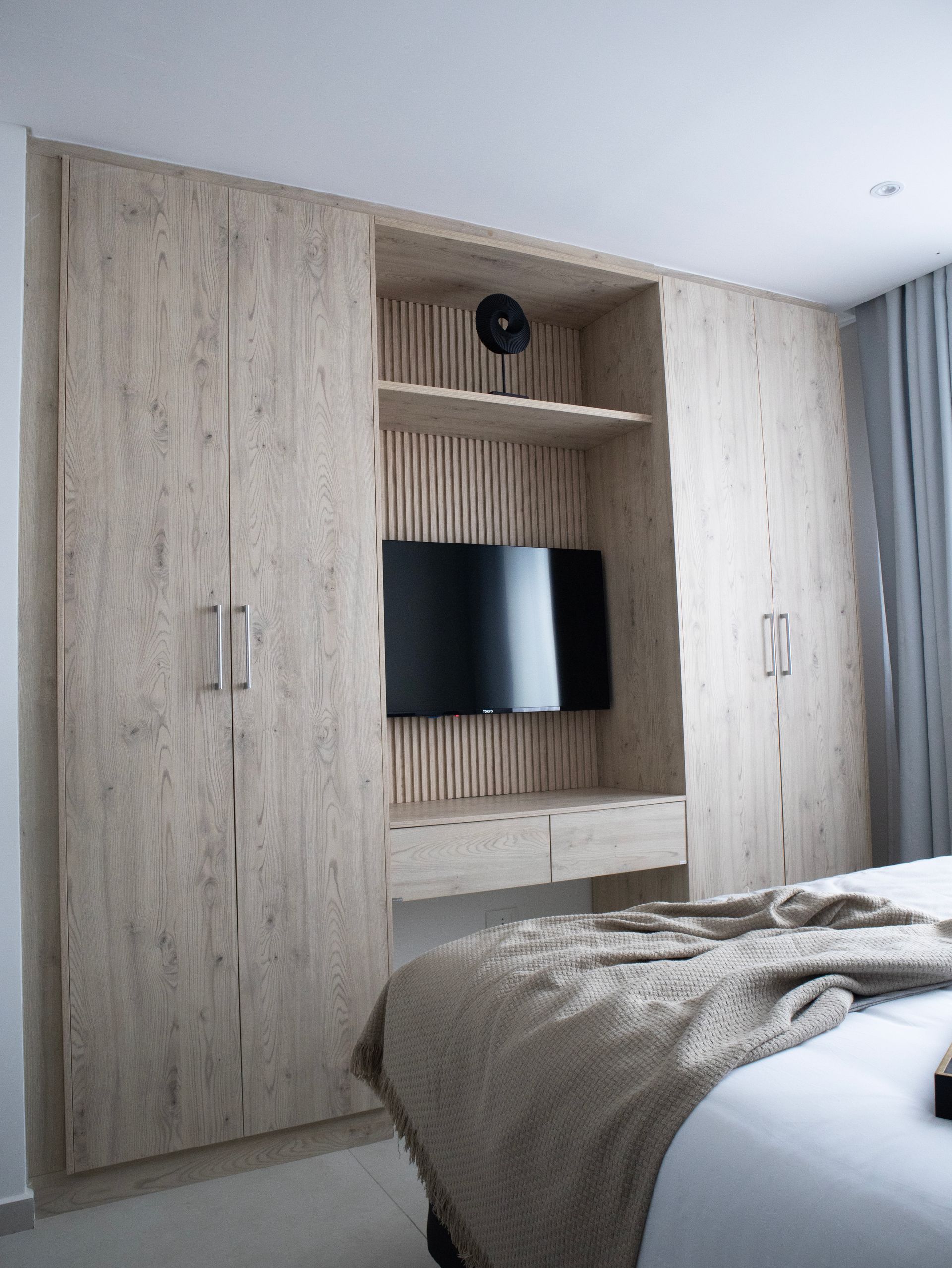 Armario empotrado de madera con TV en un dormitorio, delante del armario hay una cama.