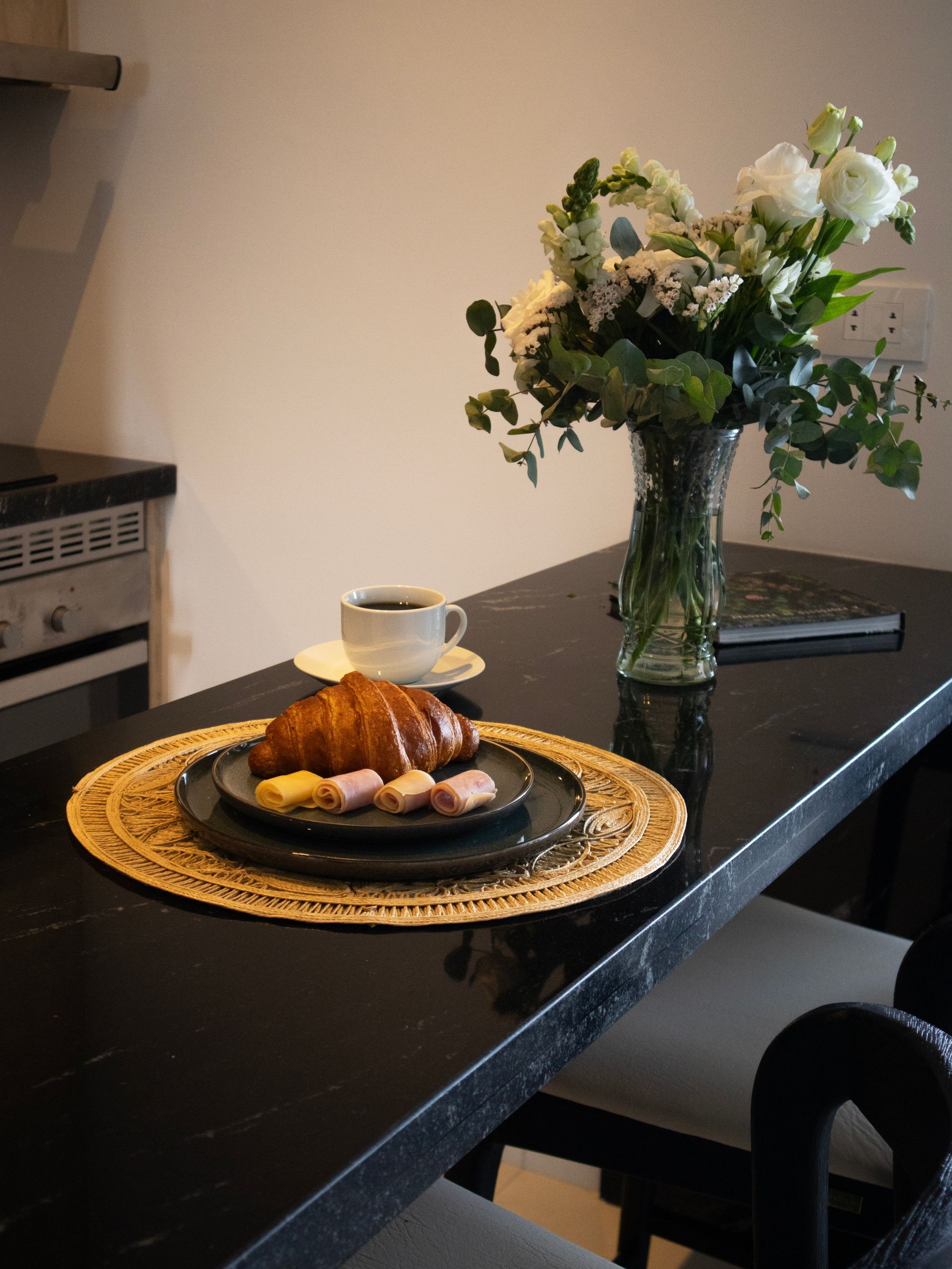 Escena del desayuno: croissant, café, flores, sobre mesa negra, en la cocina.